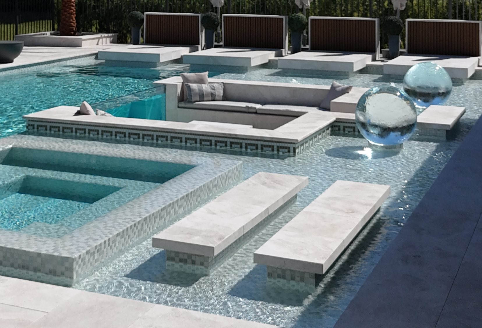 The sunken lounge inside the pool: cushions, Greek-key mosaic band and the raised spa behind