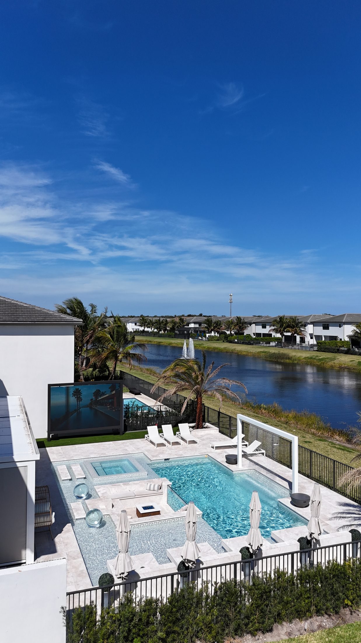Elevated view of the backyard with the lake beyond: pool, sunken lounge, outdoor cinema and pergola