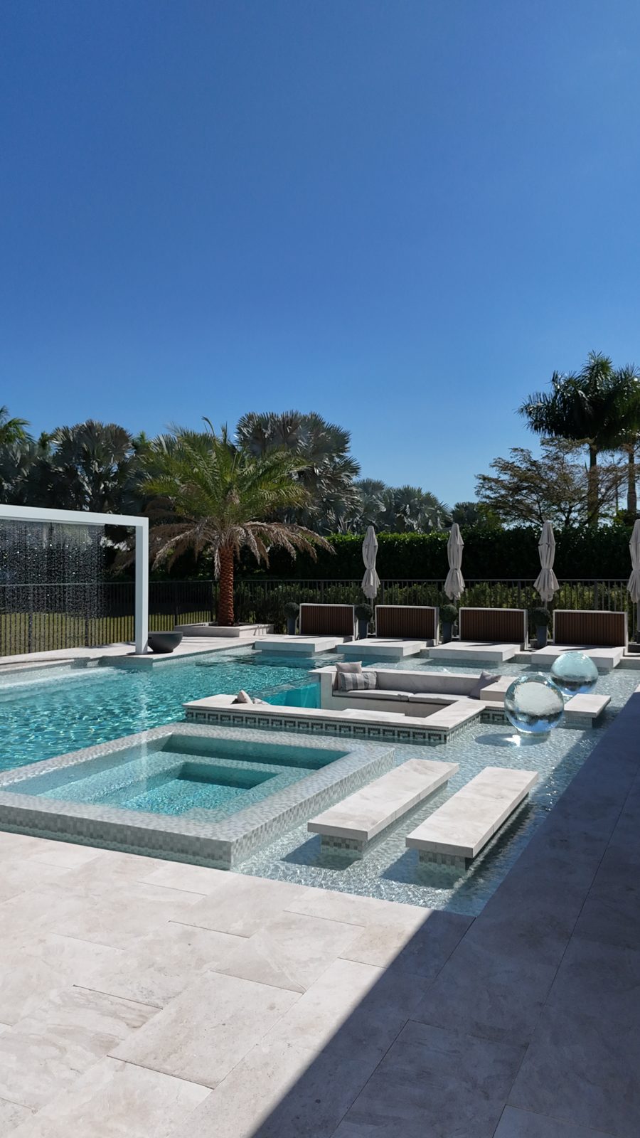 The finished pool: raised spa, sunken lounge with daybeds, crystal sphere and the rain-curtain portal at the lake end