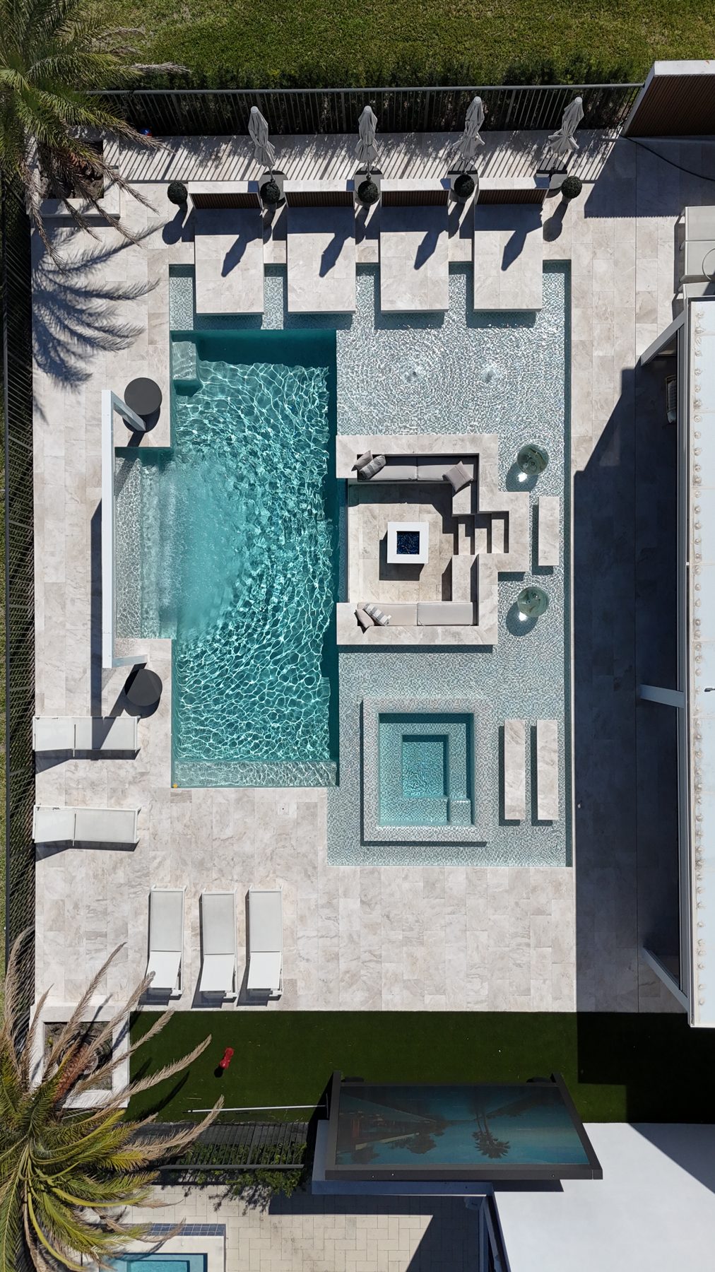 Drone view straight down: pool, sunshelf with daybeds, sunken lounge, raised spa and the marble deck