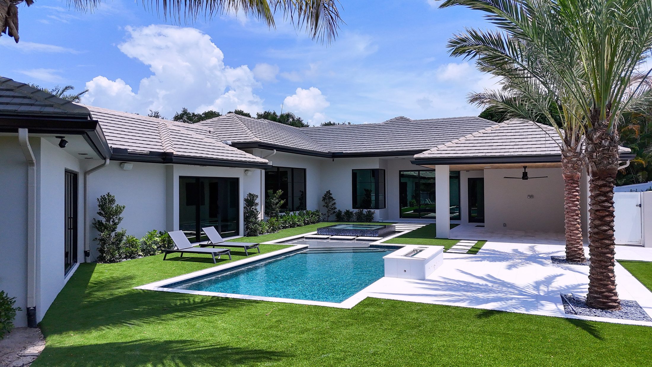 Completed backyard in Delray Beach: pool with raised spa, sunshelf, fire-and-water table, marble deck and artificial turf