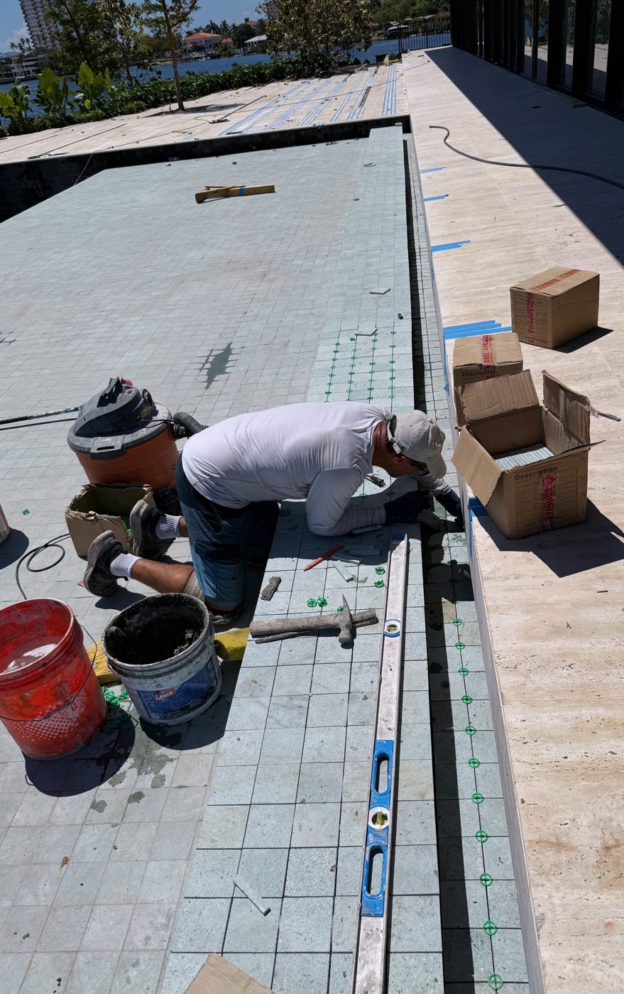 Mason setting travertine coping on the raised wall