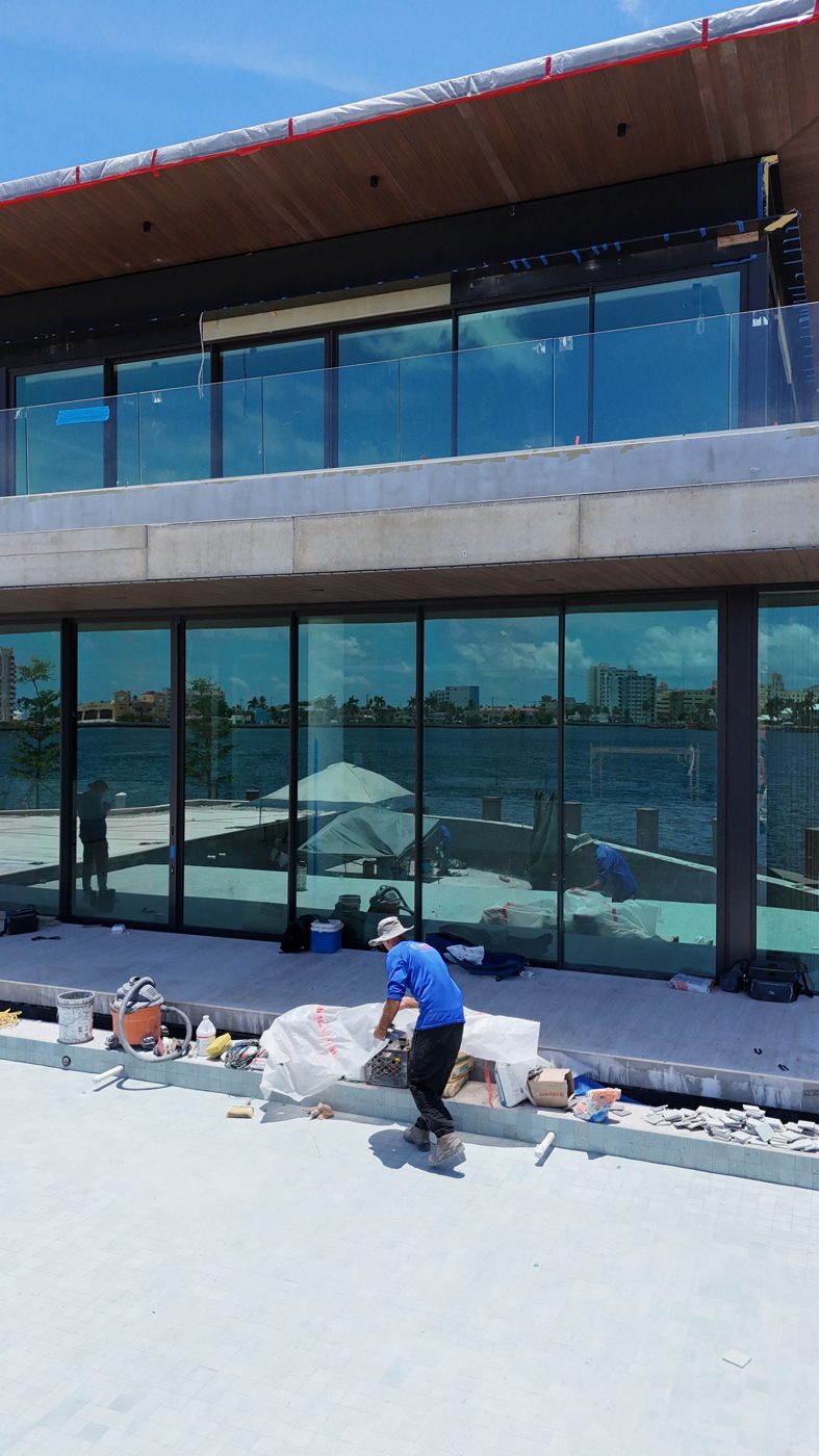Glass-walled residence seen from the pool deck during construction