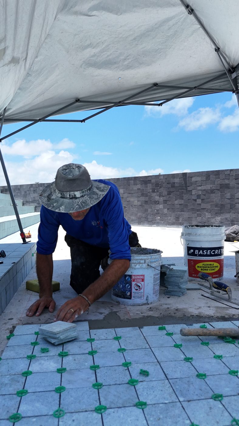 Tile setter installing emerald porcelain tile on the pool floor