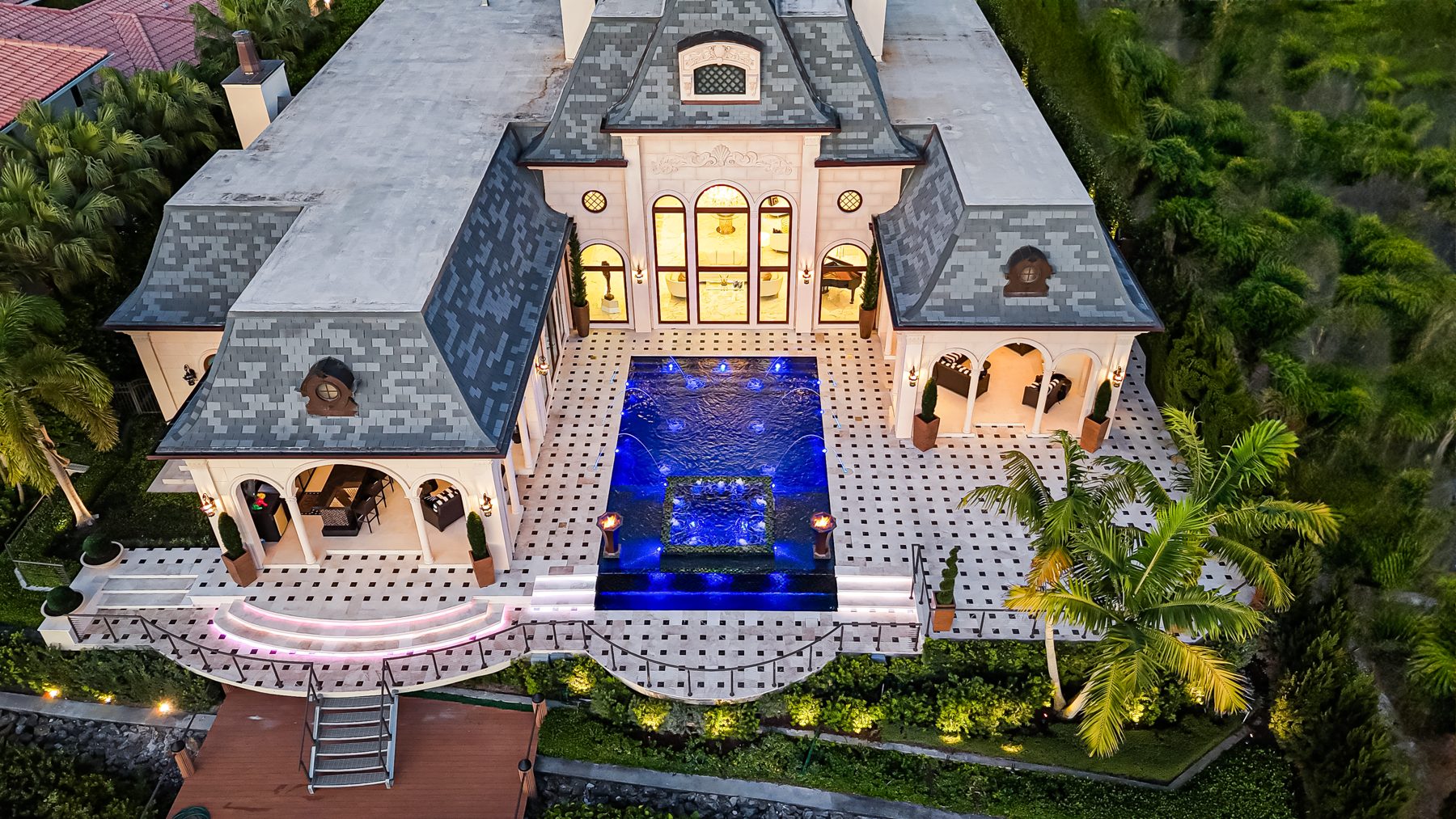 Night aerial of the pool glowing blue between the wings of the estate