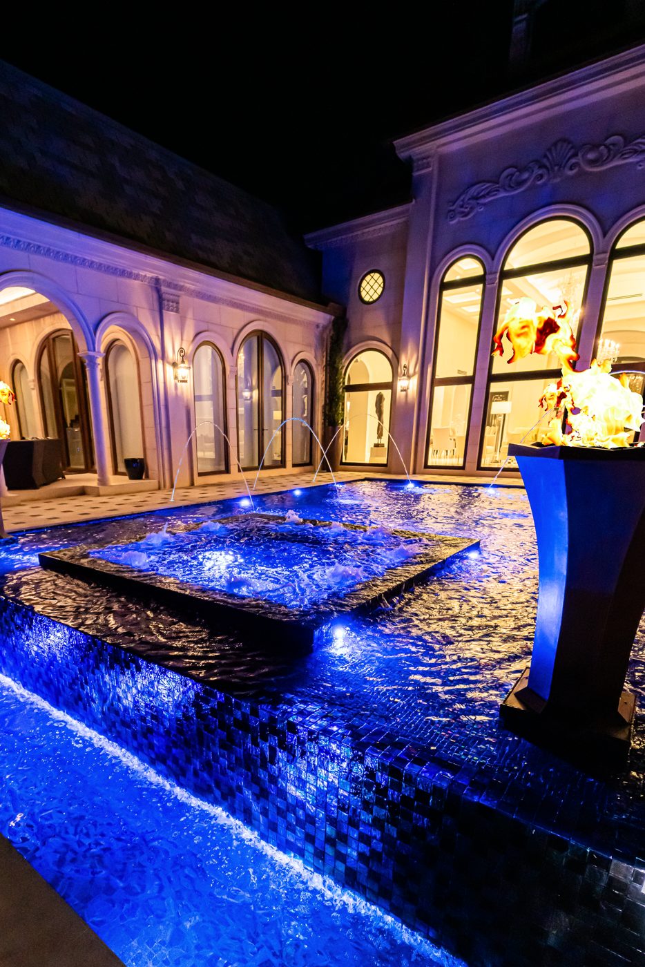Night view along the pool edge with the lit arches of the house